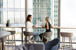 © fizkes - Two women engaged in conversation, ideas sharing and opinion exchanging, working on joint task or project met in modern skyscraper office with downtown cityscape view through window. Business meeting