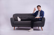 © NETI studio - Full body image of young Asian man posing on sofa on white background