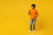© ViDi Studio - Full body young smiling happy Indian man he wears orange t-shirt casual clothes hold in hand use mobile cell phone chat online isolated on plain yellow background studio portrait. Lifestyle concept.