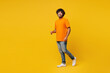 © ViDi Studio - Full body side view fun smiling happy cheerful young Indian man he wearing orange t-shirt casual clothes walk go looking camera isolated on plain yellow background studio portrait. Lifestyle concept.