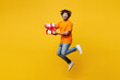 © ViDi Studio - Full body young surprised Indian man wear orange t-shirt casual clothes jump high hold in hand present box with gift ribbon bow isolated on plain yellow background studio portrait. Lifestyle concept.