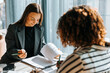 © Maskot - Female business professional reviewing contract while sitting with client at office