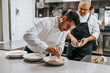 © Maskot - Young male chef grating cheese on dumpling plate while garnishing at countertop in kitchen