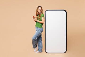 Wall Mural - Full body side view happy young woman wear green t-shirt casual clothes big huge blank screen mobile cell phone with workspace area using smartphone isolated on plain pastel light beige background.