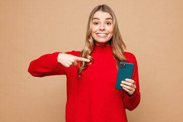 Wall Mural - Young shocked surprised woman she wear red casual clothes hold in hand use point index finger on mobile cell phone isolated on plain pastel light beige background studio portrait. Lifestyle concept.