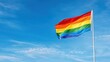 © TJ.Creative - Rainbow flag waving in the wind against a clear blue sky representing diversity and inclusion