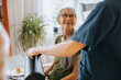 © Maskot - Smiling senior woman sitting at dining table and talking with nurse at care home