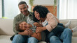© Yuliia - Bonding family African American parents with little adopted kid boy son tickling on home sofa playing together sincere laugh having fun happy childhood adorable playful child boy kidding with mum dad