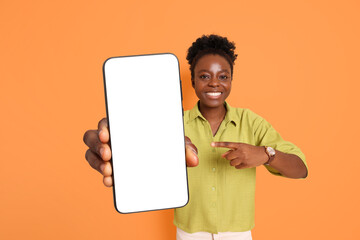 Happy woman pointing at mobile phone with blank screen on orange background. Mockup for design