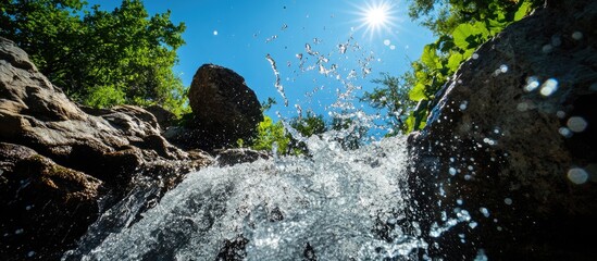 Poster - Waterfall with splashes under bright sunlight surrounded by lush greenery and rocks with clear blue sky Copy Space