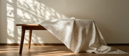 Poster - wooden table draped with elegant white fabric casting soft shadows on the wall in a minimalist inter