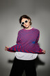 © LIGHTFIELD STUDIOS - Handsome young man poses confidently in a colorful striped sweater and cool sunglasses.