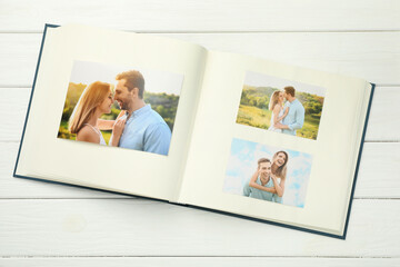 Different photos in open photo album on white wooden table, top view