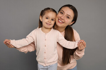 Wall Mural - Portrait of happy mother and her cute little daughter on grey background