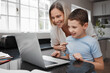 © peopleimages.com - Mother, child and laptop in kitchen for learning, educational platform and streaming tutorial. Woman, kid and computer in home for homework notes, video call or communication for online lesson course
