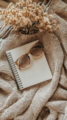 Poster - A tranquil indoor setup featuring a soft, textured blanket, an open blank notebook ready for thoughts, and chic sunglasses resting nearby, complemented by a delicate flower arrangement