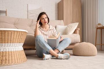 Wall Mural - Young pretty woman reading book and sitting on floor near sofa in living room