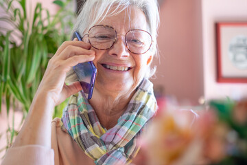 Wall Mural - Portrait of senior woman in eyeglasses sitting at cafe table using smart phone, elderly lady smiling talking on cellphone