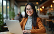 © D.Kaminsky - A young woman in glasses with straight light black hair of long length in a caramel brown coat sits in a cafe with a laptop