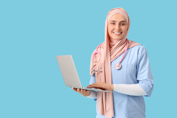 Wall Mural - Female Muslim doctor in hijab working with laptop on blue background