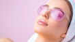 © Phatharaporn - Close up of a woman with dewy skin wearing pink sunglasses and a white towel, relaxing against a pale pink background. Soft lighting enhances her features and creates a tranquil atmosphere.