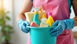 © miss irine - Housekeeper in pink apron holds cleaning supplies in turquoise bucket. Woman wearing blue gloves holds cleaning supplies like sponges, spray bottles. Indoor shot. Cleaning lady preparing for house