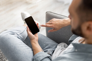 Poster - Unrecognizable young guy using smartphone with empty screen at home, mockup for website or mobile app design. Closeup of millennial man holding modern gadget, space for advertisement
