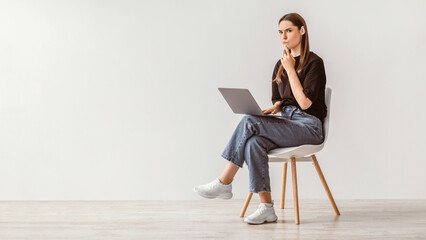 Poster - Troubled Caucasian woman sitting on chair with laptop computer, making mistake in online project, feeling stressed, thinking over solution to problem against white wall, copy space. Banner design