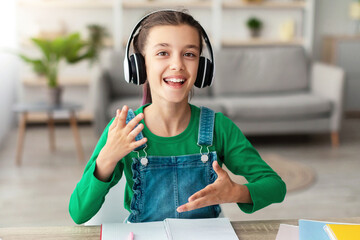Poster - Portrait of smiling girl wearing wireless headphones talking and gesturing, looking at camera, webcam point of view. Cheerful teen making video call with teacher or recording blog for social media