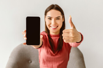 Poster - Happy Caucasian lady showing cellphone with empty screen and gesturing thumb up, recommending new mobile app or website on white studio background, mockup for advertisement