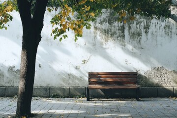 Poster - Wooden bench under a tree with autumn leaves near a weathered wall in a calm urban setting. Generative AI