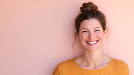 Wall Mural - Genuine Radiance: A woman with a bright, genuine smile, her hair pulled back in a messy bun, radiates joy and confidence against a soft pink background. The image conveys warmth, positivity.