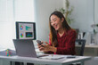 © Crystal - Asian businesswoman using smartphone and laughing at office desk
