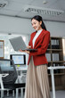 © Crystal - Asian businesswoman using laptop standing in modern office