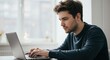 © Qstock - Focused Young Man Working on Laptop in Modern Home Office Setting