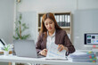 © Crystal - Asian businesswoman analyzing financial documents and working with laptop at office desk