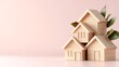 © nuiiko - Home loan estate investment concept. Wooden house models arranged creatively against a soft pink background, adorned with green leaves for a natural touch.