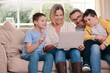 © peopleimages.com - Happy, laptop and parents with children on sofa for watching movies, online games and streaming cartoons. Family, home and mom, dad and kids on computer for subscription, bonding and internet videos