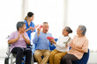 © artitwpd - Group of happy senior friends, including a woman in a wheelchair, share joyful moment while exchanging gifts in bright living room. A nurse in scrubs claps along, caregiver, celebration, companionship