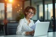 © Premium Illustration - Smiling young woman with glasses and curly hair working on laptop in modern office with warm sunlight and blurred background for business, technology, remote work, productivity