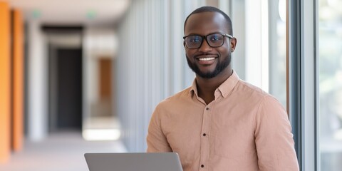 Wall Mural - A man wearing glasses and a striped shirt is smiling and holding a laptop. Concept of confidence and professionalism, as the man is comfortable using technology in a public setting