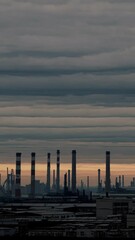 Poster - A desaturated shot of an industrial skyline with smokestacks silhouetted against a cloudy sunset, the air thick with haze and grit.