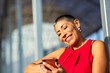 © Paula - Woman with a shaved hairstyle and bright red blouse using phone while smiling outdoors