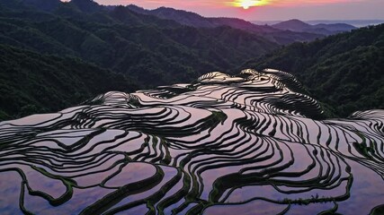 Aufkleber - An aerial perspective of terraced rice paddies at sunset, each flooded level mirroring the sky in a patchwork of orange and gold.