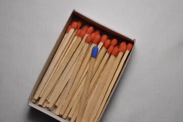 Wall Mural - A lone blue match contrasts beautifully against a sea of orange matchsticks within a cardboard box.