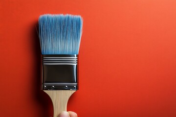 Poster - Brush held against vibrant orange wall ready for painting and creative expression
