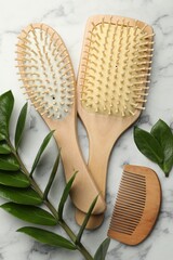 Wall Mural - Wooden hair brushes, comb and green leaves on white marble table, flat lay