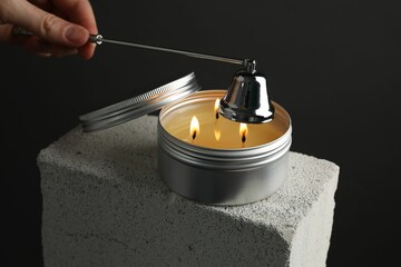 Wall Mural - Woman extinguishing burning soy wax candle with snuffer against gray background, closeup