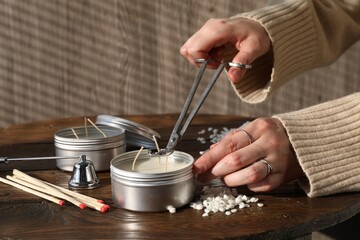 Wall Mural - Woman cutting soy candle wick with trimmer at wooden table, closeup