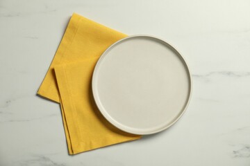 Wall Mural - Yellow napkin and empty plate on white marble table, top view